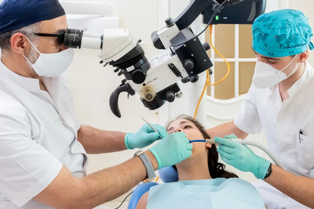 Due odontoiatri di dentisti-coppede-medical-hub eseguono una procedura odontoiatrica su un paziente utilizzando strumenti specializzati e un microscopio dentale in un ambiente clinico.