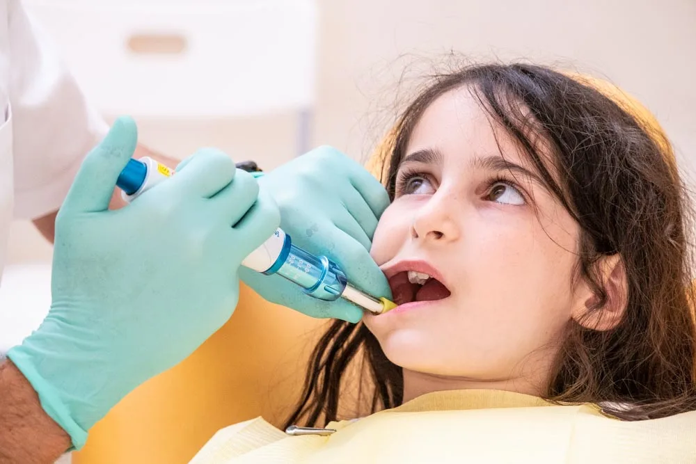 Un dentista dell'odontoiatria-pediatrica-coppede-medical-hub-roma, indossando guanti verdi, esamina attentamente i denti di una bambina che siede comodamente sulla poltrona.