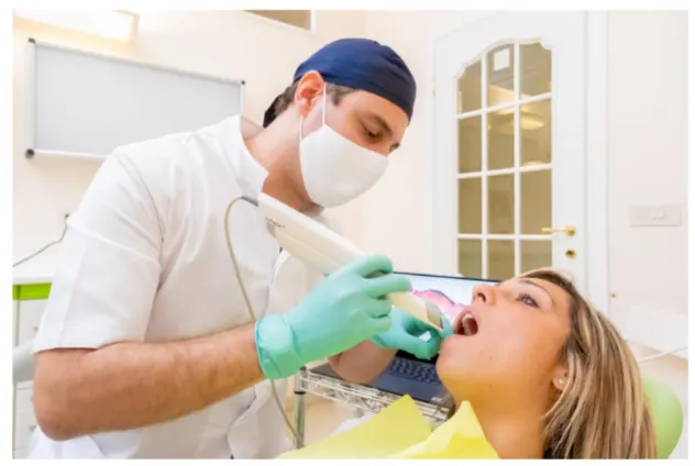 Un dentista di protesi-dentale-coppede-medical-hub-roma, indossando guanti e mascherina, utilizza uno scanner dentale su una paziente donna comodamente sdraiata sulla poltrona.