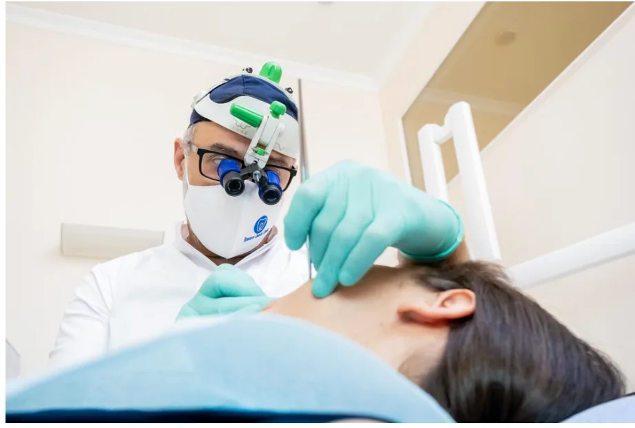 Un medico dell'odontoiatria-conservativa-coppede-medical-hub-roma, con occhiali di ingrandimento e guanti, esamina un paziente sdraiato in un ambiente clinico.