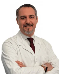 Il Dott. Edoardo Brauner del Coppedè Medical Hub di Roma, un uomo con capelli corti e scuri e pizzetto grigio, sorride in camice bianco e cravatta rossa, incrociando le braccia su uno sfondo bianco.