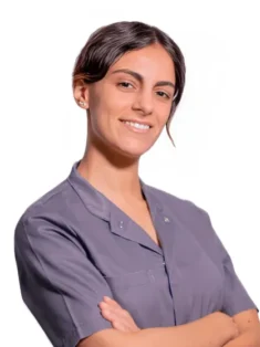 La Dott.ssa Giulia Amelina del Coppedè Medical Hub di Roma, una donna dai capelli scuri in camicia grigia, sta in piedi con le braccia incrociate, sorridendo con sicurezza su uno sfondo bianco.