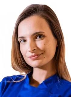 La Dott.ssa Roberta Carlini Coppedè è ritratta con capelli lisci e castani, indossa un top blu royal e sorride dolcemente. Ha un segno di bellezza sulla guancia ed è in posa su un semplice sfondo bianco presso il Medical Hub di Roma.