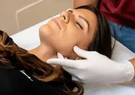 Una persona con i guanti esamina la mascella di una donna sdraiata su un tavolo da visita con gli occhi chiusi presso fisioterapia-coppede-medical-hub.