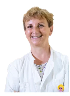 La Prof.ssa Maria Teresa Fadda, una persona sorridente con i capelli corti, indossa un camice bianco e una camicia a fantasia, in posa su uno sfondo bianco semplice.