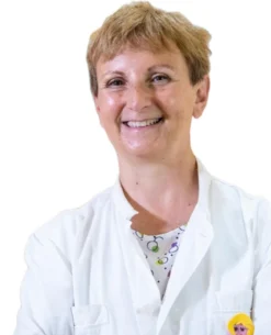 La Prof.ssa Maria Teresa Fadda, una persona sorridente con i capelli corti, indossa un camice bianco e una camicia a fantasia, in posa su uno sfondo bianco semplice.
