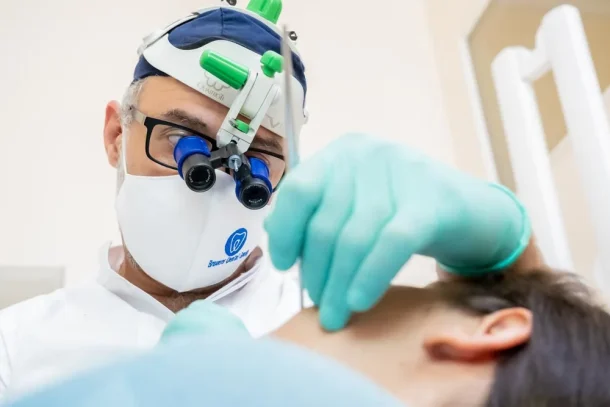 Un dentista con lenti di ingrandimento e guanti esamina un paziente sdraiato su una poltrona odontoiatrica durante una visita-dentistica-coppede-medical-hub-roma.